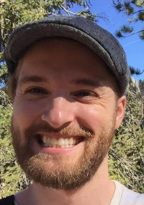 Jordon Lakoduk smiles at the camera. He is wearing a short brimmed cap and has a beard.